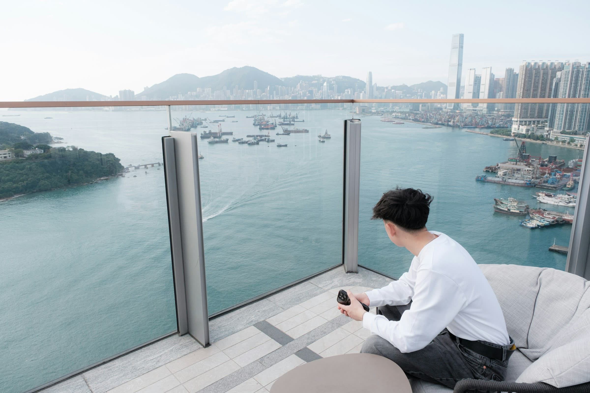 Un homme installé sur son balcon face à la baie, téléphone à la main